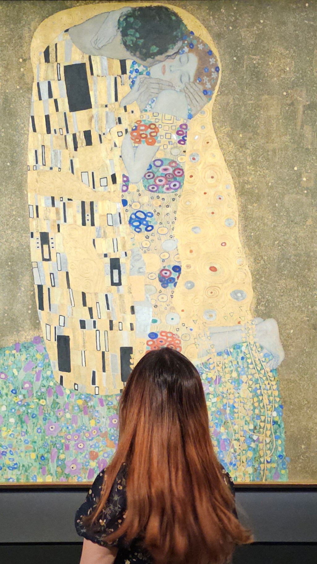 The Klimt shines in the background, in the lower front Melissa's head is in the center her face is hidden as she is looking at the painting.